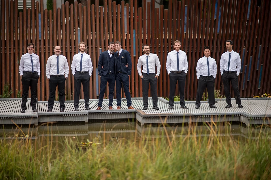 the wedding party stands together on a dock at LGBT Wedding Photographer Robert Knapp at ​Tanner Springs Park in Portland Oregon