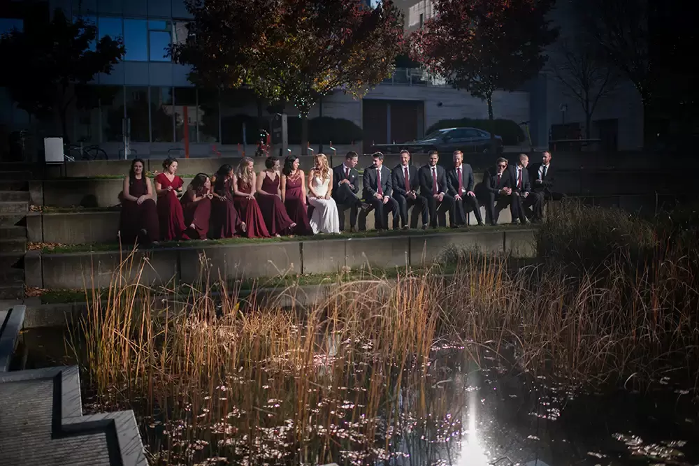 Wedding Photographers in Portland  at the EcoTrust Robert Knapp Photographer the wedding party sit on the steps in the park. they sit together in a beam of light reflected from a tall building. The lighting effect drops the exposure for the surrounding area leaving only them in the light. 