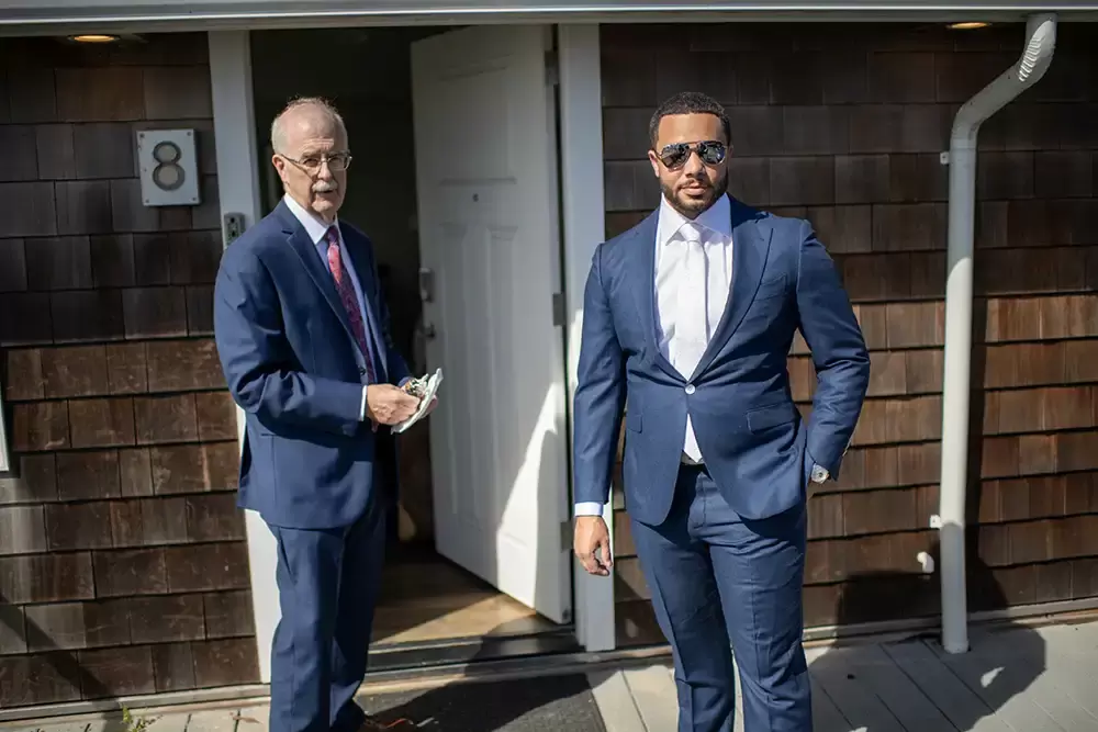 groom stands with father outside the beach house