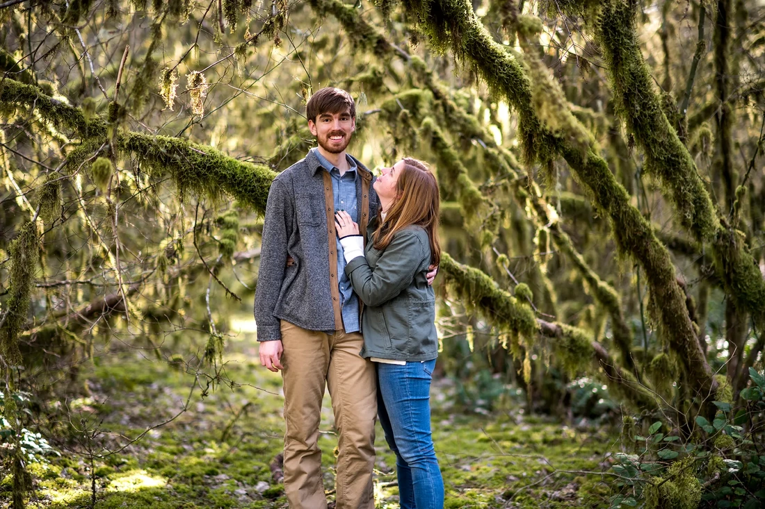 ​Winter Waterfall Engagement Photos from Photographer Robert Knapp A couple stand in the mossy under brush of an old growth forest 