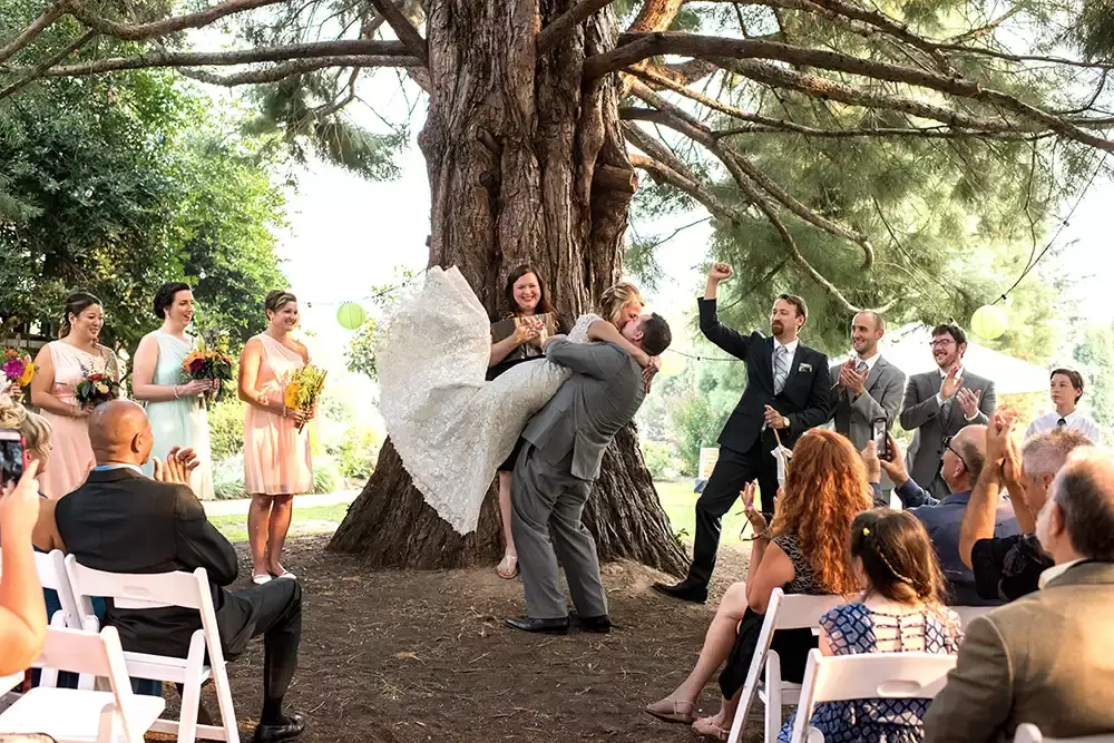Portland Wedding Photographer Robert Knapp Catches this kiss at the end of the ceremony. The groom has lifted the bride off the ground completely. The dress is flying perfectly as if she were walking. Everyone is cheering.
