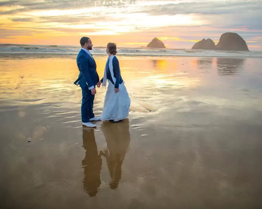 Portland Wedding Photographer Robert Knapp photographs this couple at sunset in Oceanside Oregon. The sunset, islands in the distance, the couple all reflect in the wet sand like a rough mirror. 