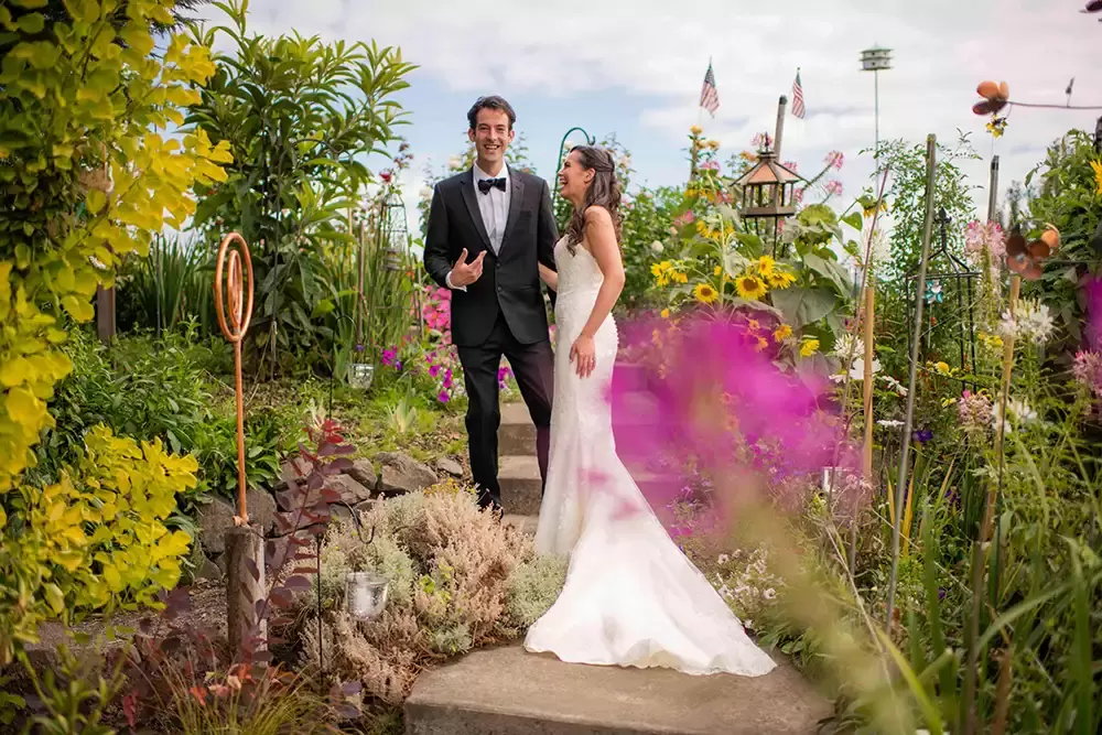 Portland Wedding Photographer Robert Knapp Photographs a first look for a couple standing in a flower garden. The photo is very busy with flowers and bird houses, feeders and garden art. 