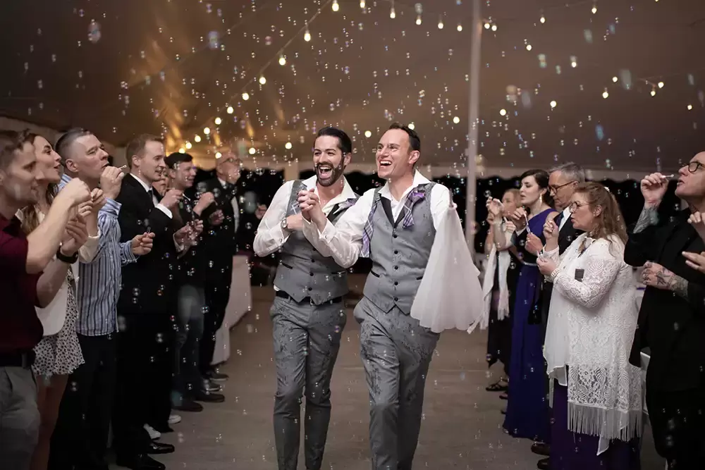 Portland Wedding Photographer Robert Knapp photographs two grooms skipping though a cloud of bubbles and twinkling lights on a rainy wedding night, happier than ever. 