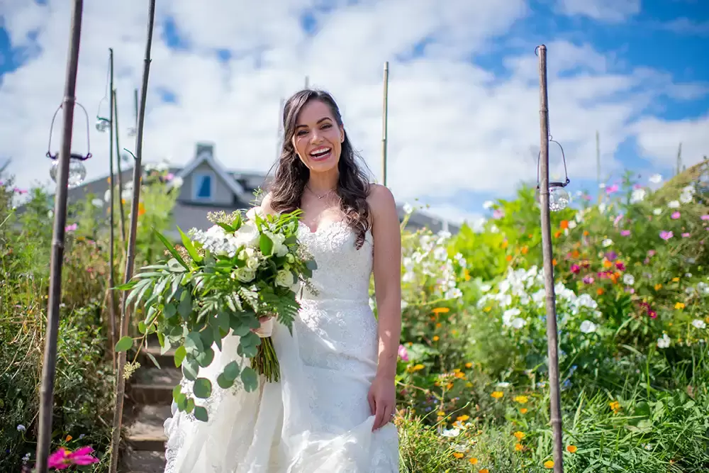 bride stands in a flower garden with her bouquet under a blue sky with some clouds A ​Sauvie Island Wedding from Photographer ​Robert Knapp 