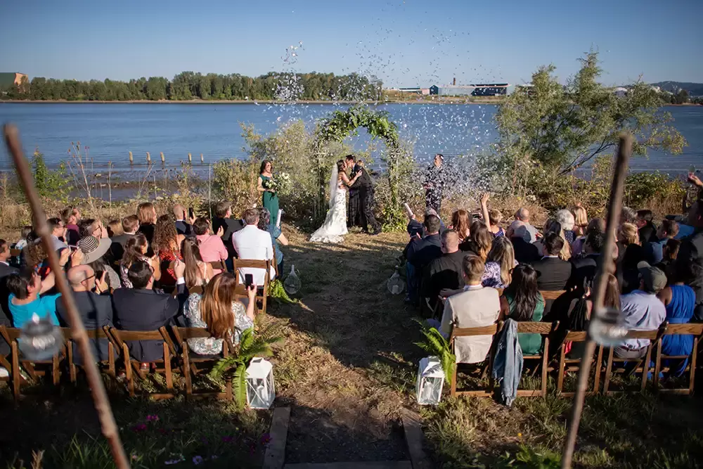 the bride and groom kiss at the end of the ceremony. All the guest through flower petals in the air at A ​Sauvie Island Wedding from Photographer ​Robert Knapp 