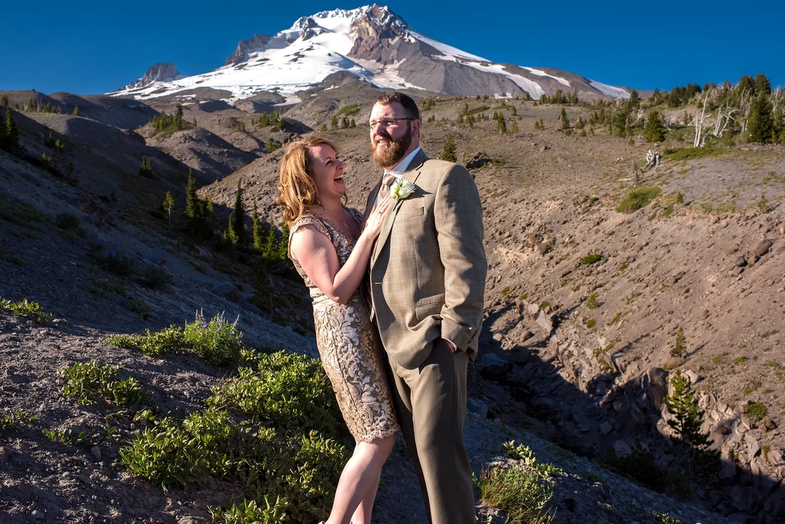 Bride and groom laugh in front of a massive mountain covered with glaciers from a Wedding at Timberline Lodge