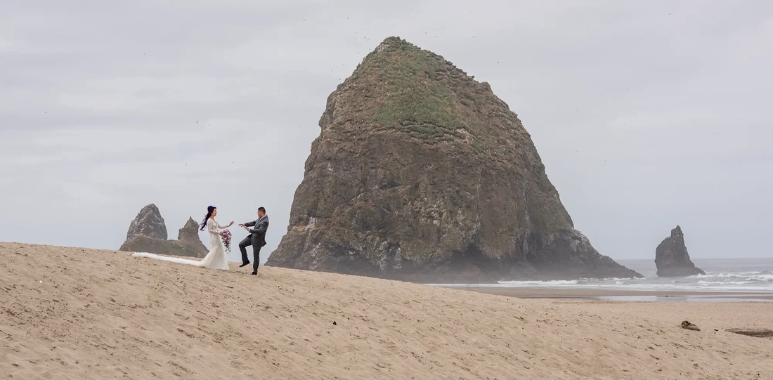 Bridal Photos at Cannon Beach by Photographer Robert Knapp a couple play in the sand in front of haystack rock.