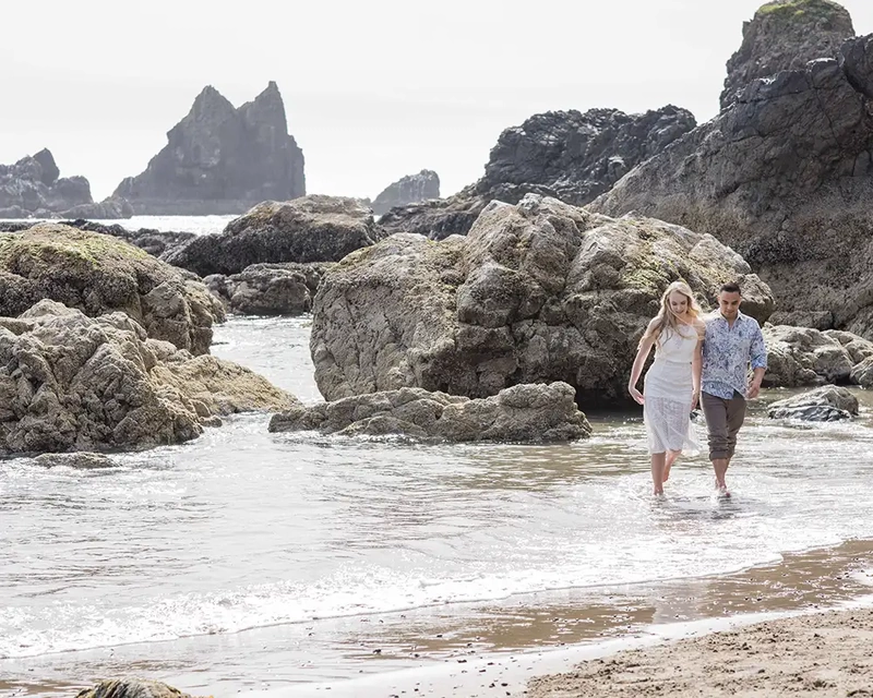 couple walks in the ocean and holds hands Cannon Beach Engagement Photos With Photographer Robert Knapp