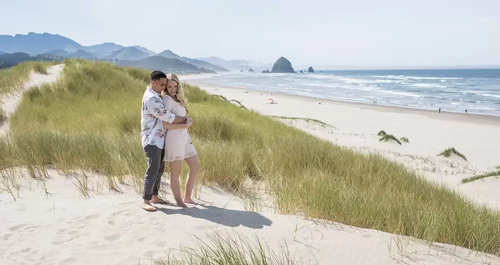a couple stands on a sand dune overlooking Cannon Beach Engagement Photos With Photographer Robert Knapp