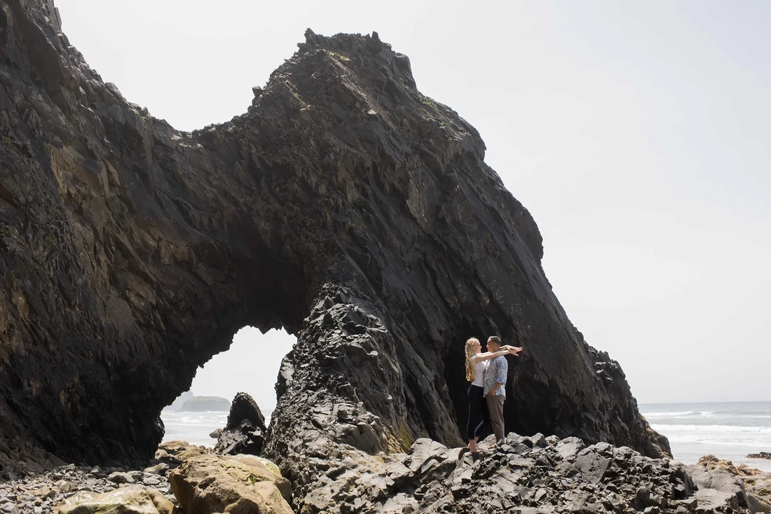 Cannon Beach engagement photos a couple stands on the rock next to the ocean. The photo is amazing.