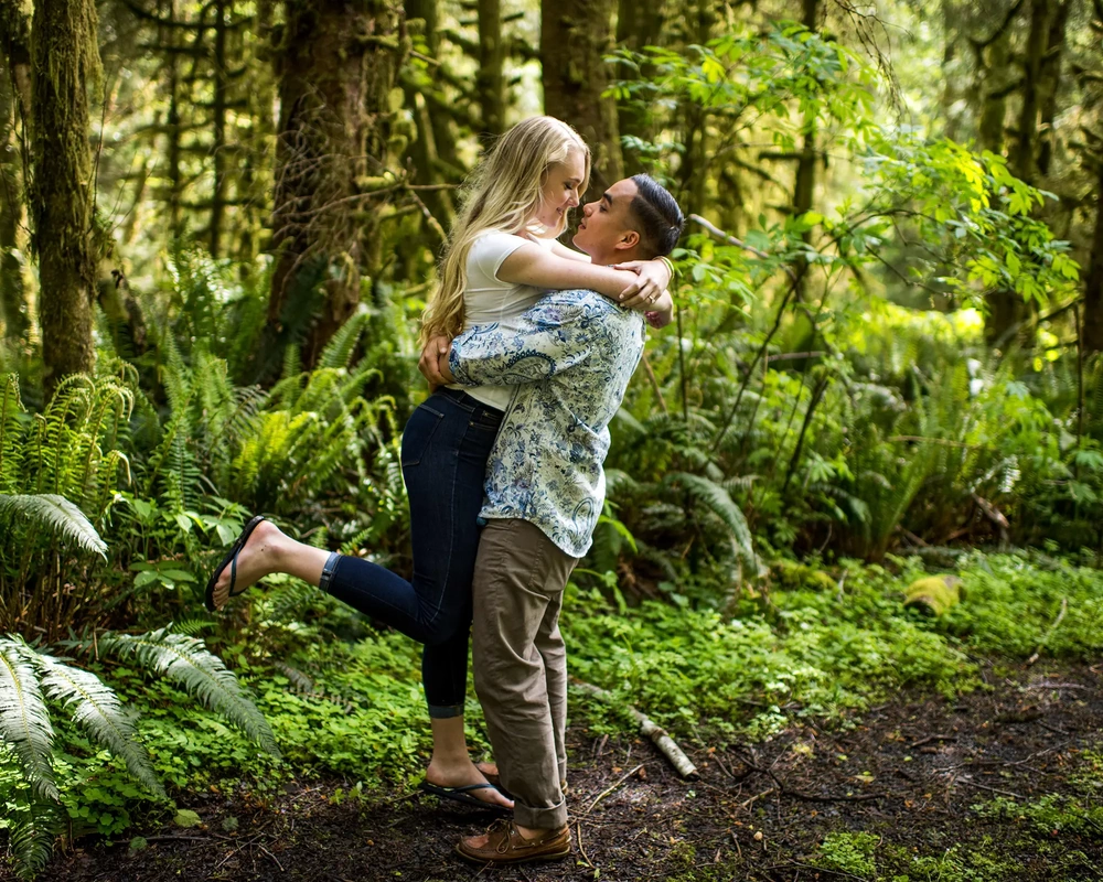 Cannon Beach Engagement Photos, A man lifts a woman off the ground on a path in the woods above the beach