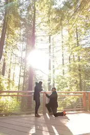 Photographers Portland at The Best Places to Propose in Oregon, Pictured a man on one knee with a little box in his hands, the woman cups her hands over her mouth with excitement. The sun shines through the trees the forest seems to glow