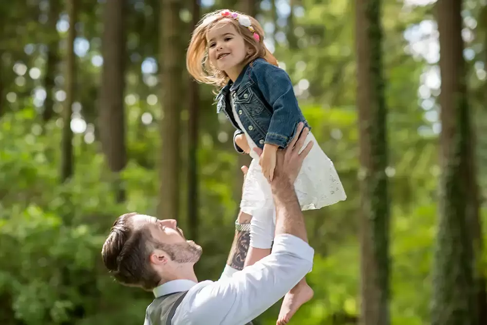father tosses daughter into the air in the woods. they both laugh Garden Photoshoot with Robert Knapp one of the highly sought after Family Photographers Portland has to offer