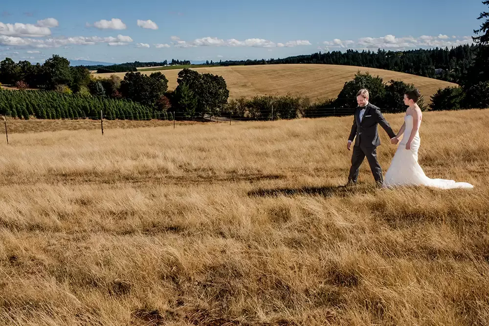 Farm Wedding Oregon
Rustic ​Chic Style with Robert Knapp Photographer An interesting image of a bride and groom walking across a field. The sky is a soft light blue. Just above the horizon a line of little white clouds. In a Tux and Wedding dress the groom leads the bride through tall brown grasses. 