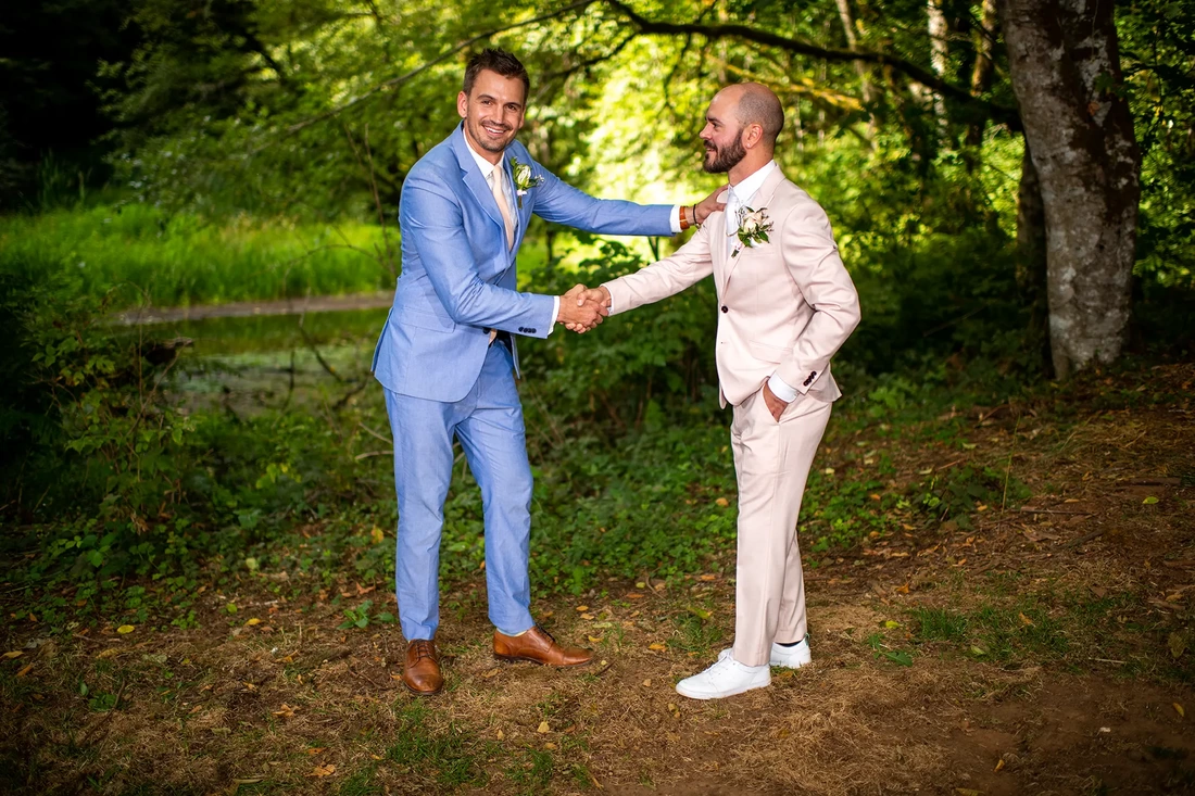 a groomsman shakes hands with the groom in the forest Beautifully lit Horning's Hideout Wedding; Modern Art Photograph