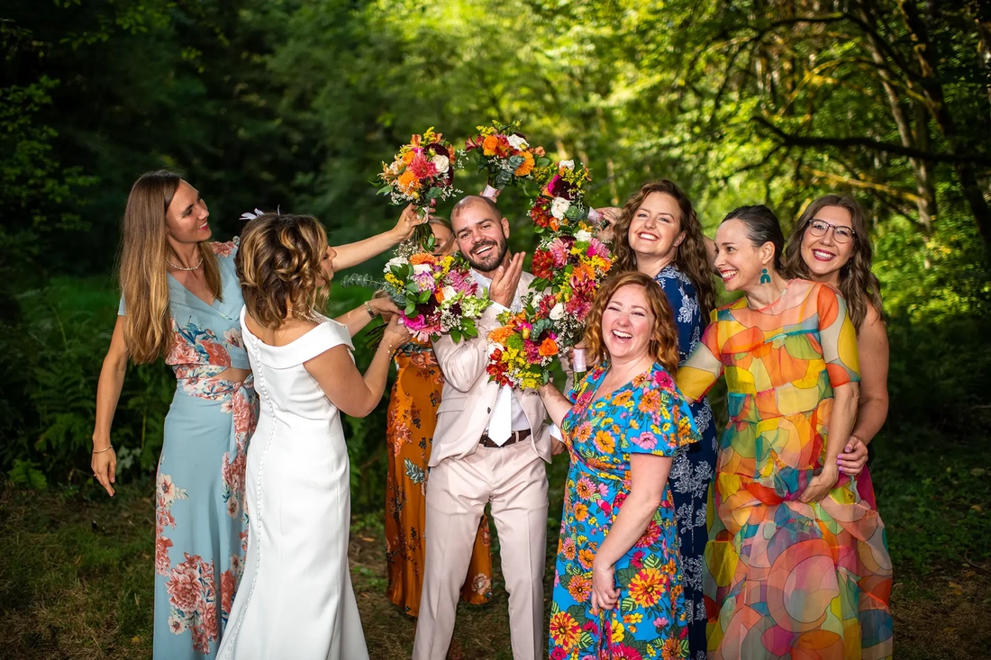 bridesmaids surround the groom with their bouquets, the groom makes a fun lighthearted smile Beautifully lit Horning's Hideout Wedding; Modern Art Photograph