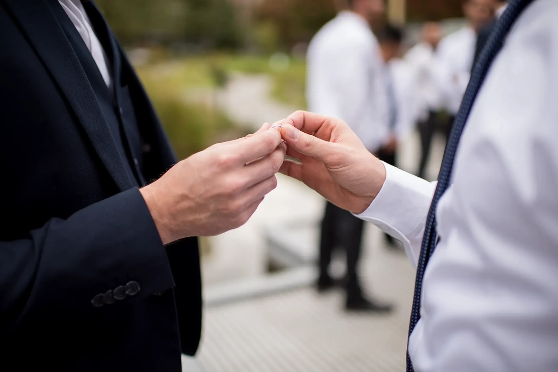 the groom passes a ring to the best man LGBT Wedding Photographer Robert Knapp at ​Tanner Springs Park in Portland Oregon