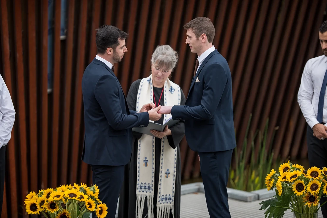 groom puts a ring on the other groom LGBT Wedding Photographer Robert Knapp at ​Tanner Springs Park in Portland Oregon