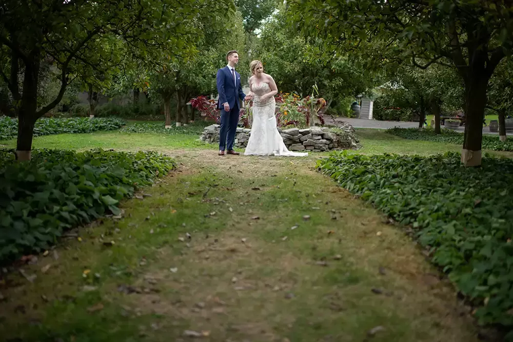 McMenamins Edgefield Weddings with Photographer Robert Knapp Bride and groom have a first look in an orchard. A grass path through the trees meets this couple in a clearing. The couple stands and looks to the distance about something curious happening. 