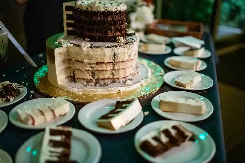 McMenamins Edgefield Weddings with Photographer Robert Knapp the cake has been cut. the top tier is gone. The two remaining tiers are chocolate and vanilla with what looks like raspberry and cream frosting. The table is covered with servings of cake. 