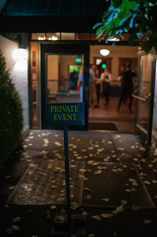 McMenamins Edgefield Weddings with Photographer Robert Knapp A sign that reads private event stands in front of an open door. Behind the open door the dance floor is covered with people dancing. Yellow fallen leafs cover the ground. 
