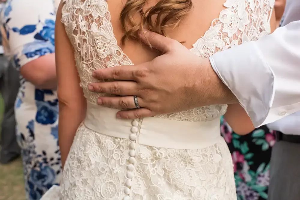 ​McMenamins Grand Lodge Weddings 
from Robert Knapp Photographer the groom sets his hand on the back of the brides wedding dress. A close up of the grooms ring and detail of the back of the lace wedding dress. 