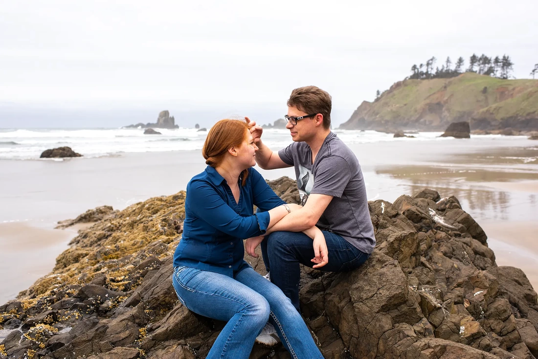 a man helps a woman with her hair. the wind is blowing it in every direction. Modern Art Photograph Engagement Photography Portland Oregon​