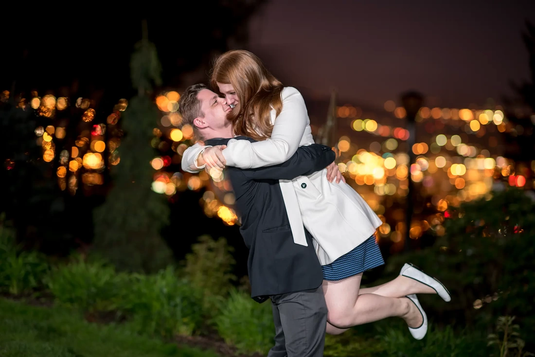 a man picks up a woman with a big hug, behind them the city of portland is out of focus Modern Art Photograph Engagement Photography Portland Oregon​