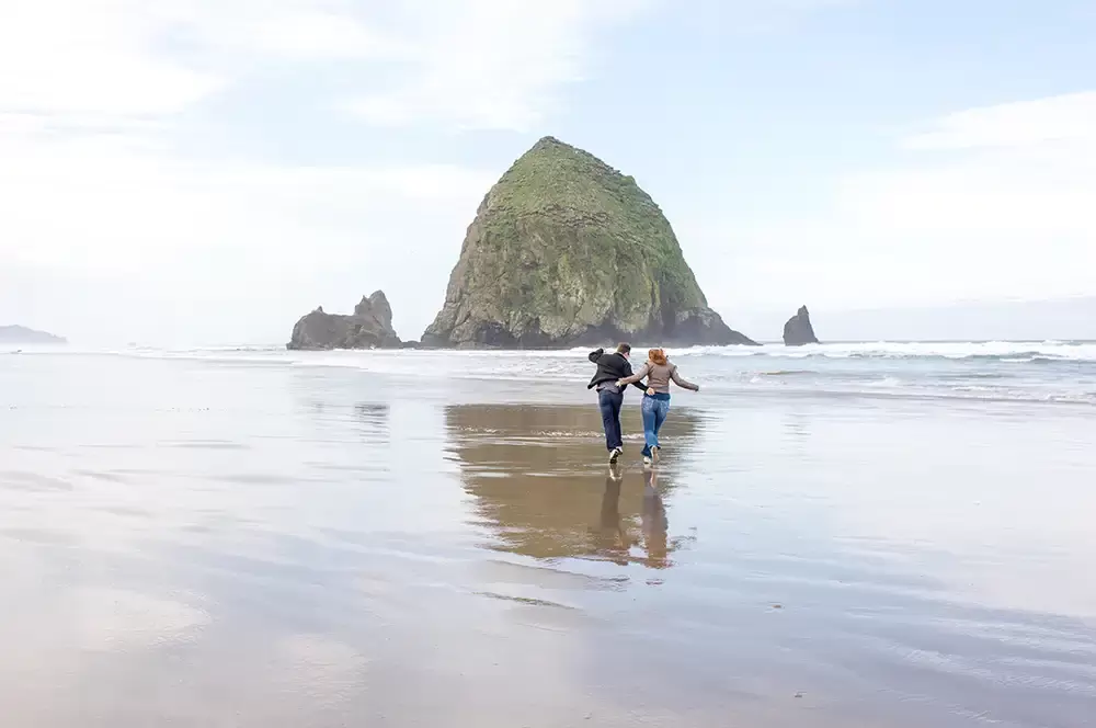 a couple runs on the beach at haystack rock. their reflection is cast in the wet sand Modern Art Photograph 
Engagement Photography Portland Oregon