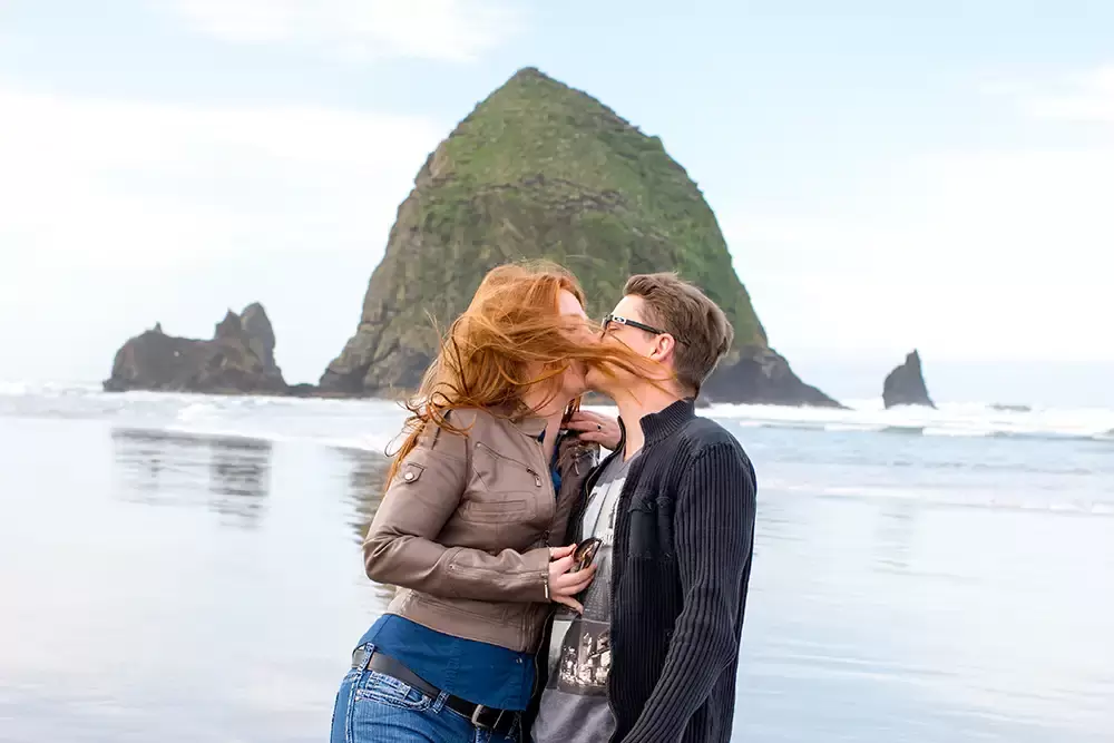 woman kisses a man on the beach, her hair is picked up by the wind and covers their faces. Modern Art Photograph 
Engagement Photography Portland Oregon