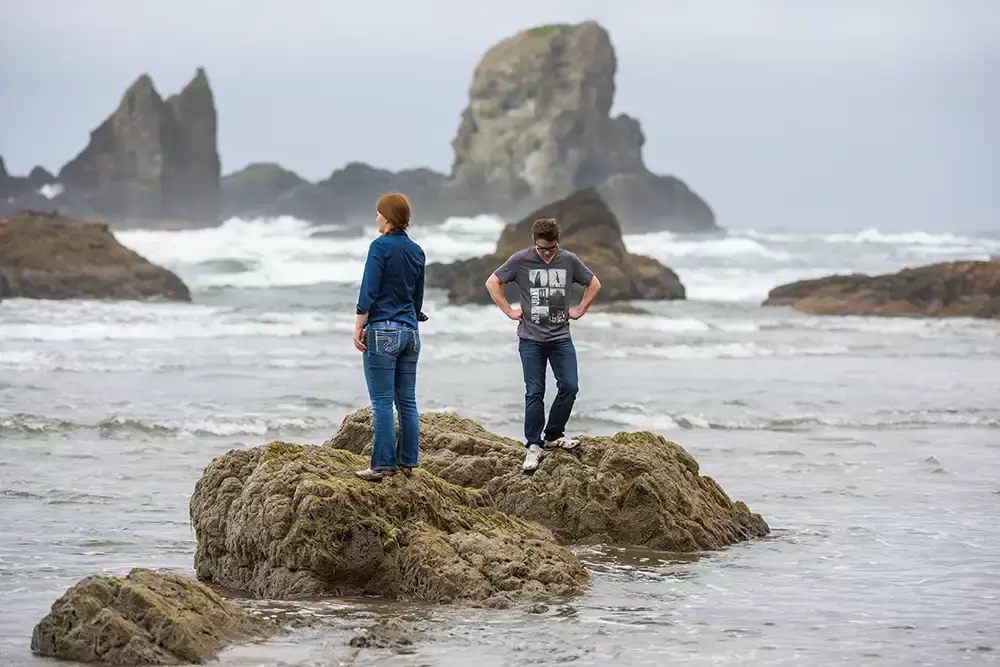 a man and woman stand on a rock. The waves have them surrounded. They are stuck for the moment. Modern Art Photograph 
Engagement Photography Portland Oregon