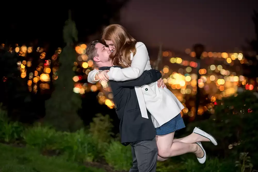 a man picks up a woman with a very big hug the city skyline on the horizon around them 