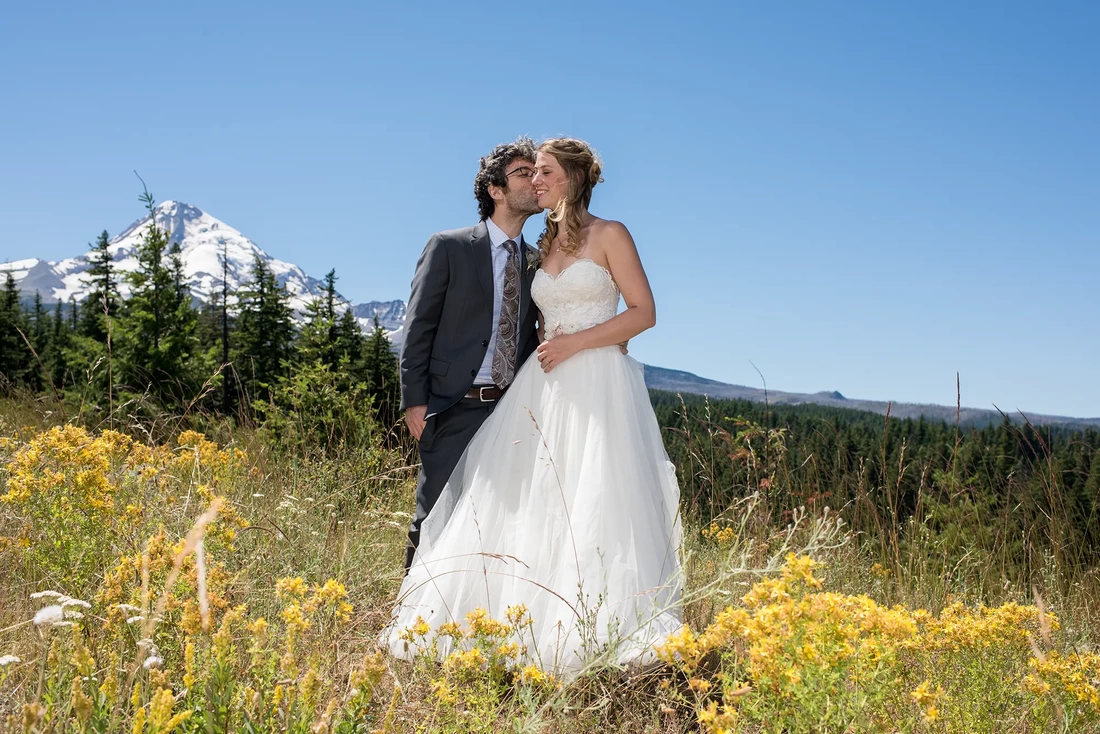 Mount Hood Weddings Capturing The Moment with Photojournalist Wedding Photographer Robert Knapp groom kisses bride on the cheek. Mt hood in the distance. Photo opportunities like this at Mount Hood Weddings are common. 
