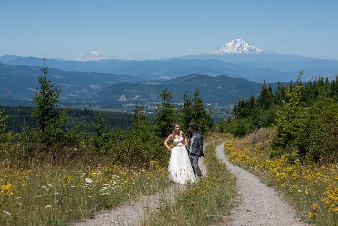 Mount Hood Weddings Capturing The Moment with Photojournalist Wedding Photographer Robert Knapp  offer terrific over the cascade mountains a bride and groom walk on a path of wildflowers with mountains in the distance