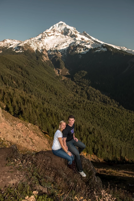 Unforgettable Moment - Mountain Engagement Photos with ​ Photojournalist Photographer Robert Knapp A couple sits perched on a rock high over a ravine. Below them a massive snow capped mountain with waterfalls crevasse and craggy peaks 