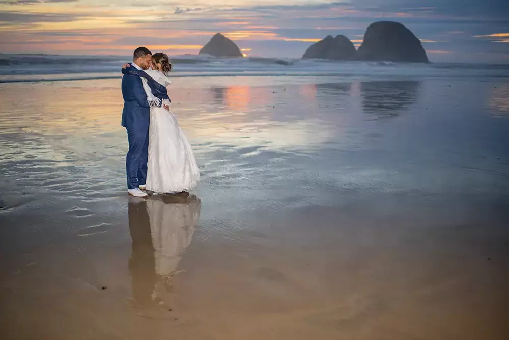 bride and groom are on the beach looking to each other in the sunset light