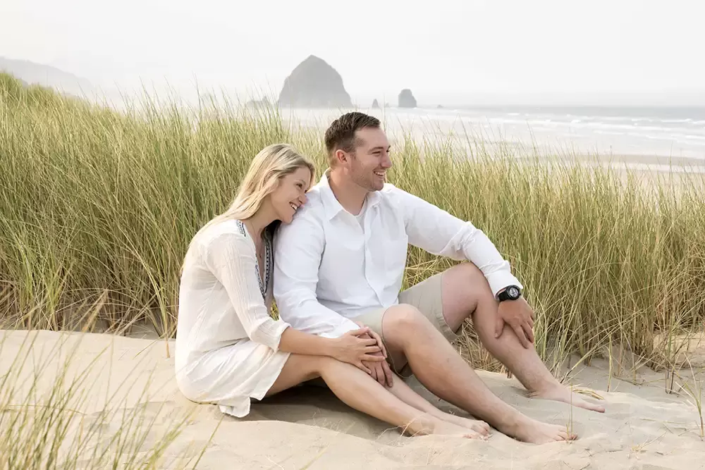 sitting in the sand on the beach a couple looks down the Oregon Coast Engagement Photos 
With 
Modern Art Photograph