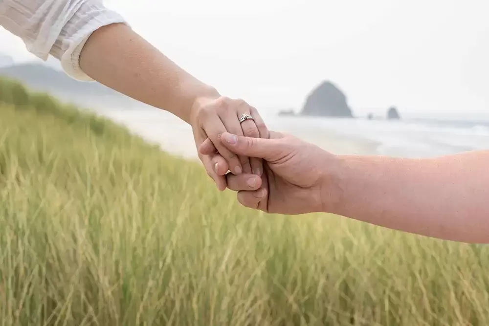 holding hands at cannon beach a couple shows off the engagement ring Oregon Coast Engagement Photos 
With 
Modern Art Photograph