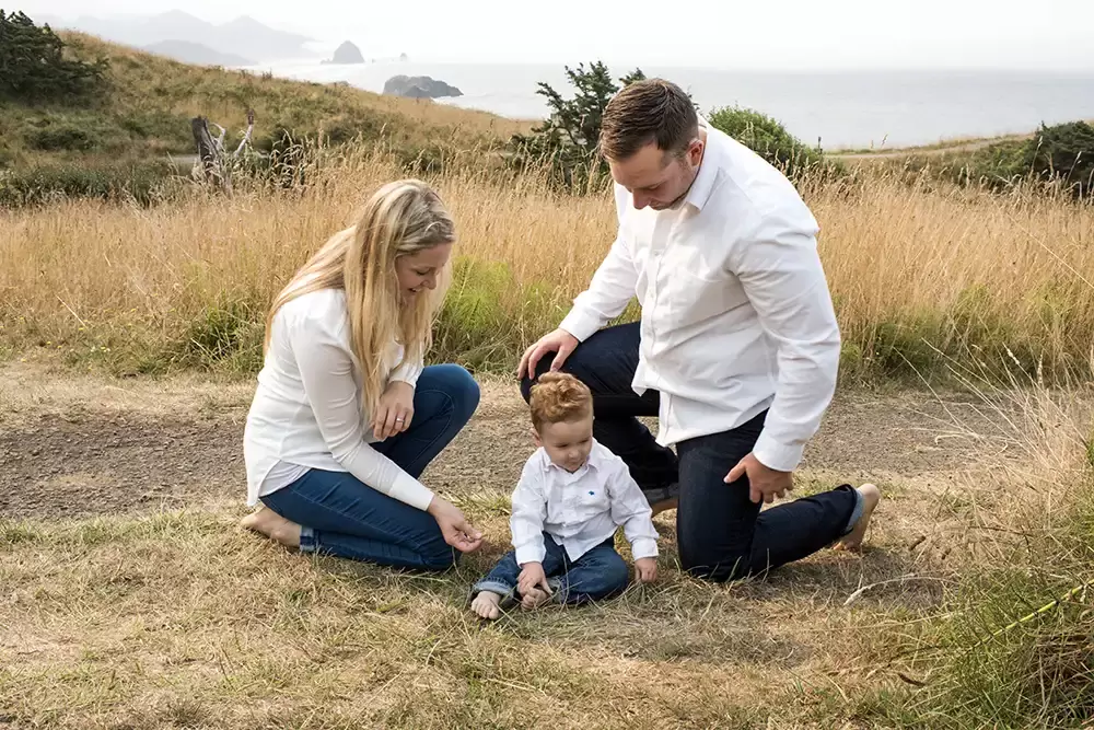 mother father and child sit in the grass together and play Oregon Coast Engagement Photos 
With 
Modern Art Photograph