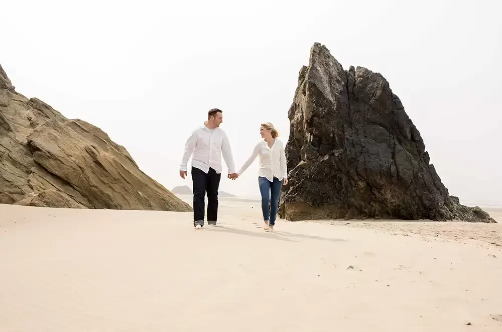 a couple walks on the sand between interesting stone features Oregon Coast Engagement Photos 
With 
Modern Art Photograph