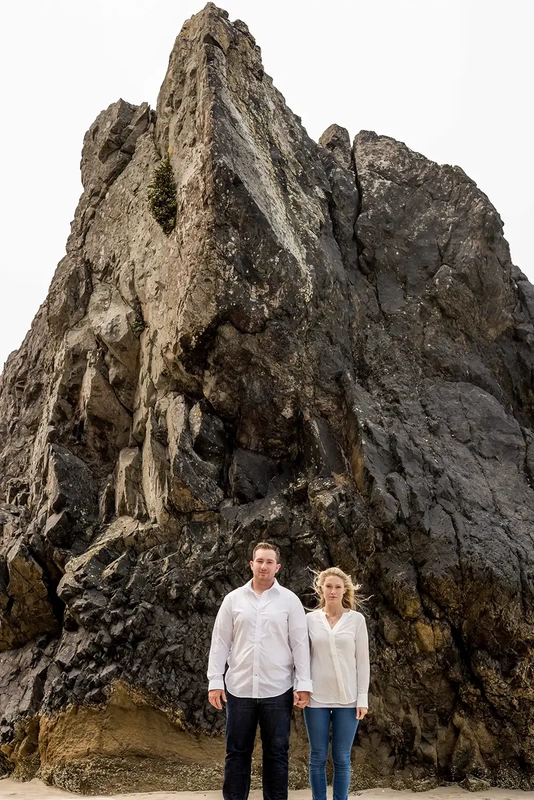 a couple Stands in front of an interesting rock feature Oregon Coast Engagement Photos 
With 
Modern Art Photograph