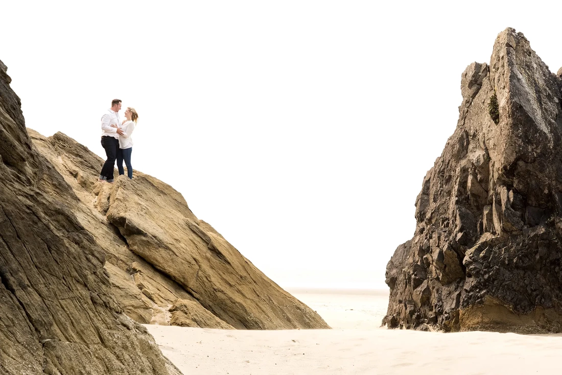 Oregon Coast Engagement Photos With Modern Art Photograph, A couple hold each other on a rock ledge over a beach