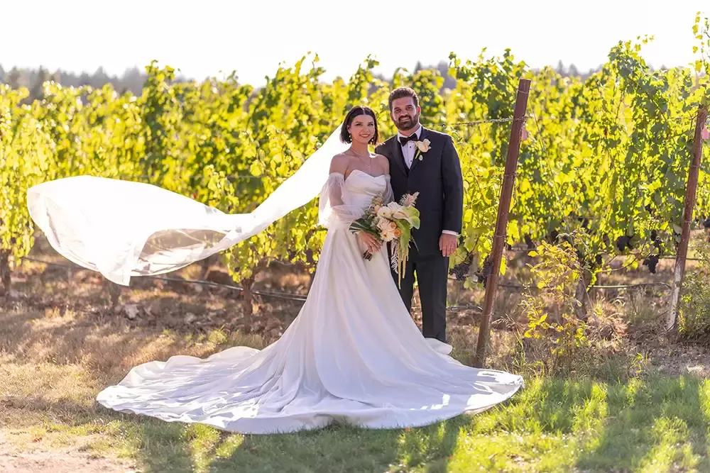 the brides veil flies in the breeze at sunset in the oregon vineyard wedding venue 