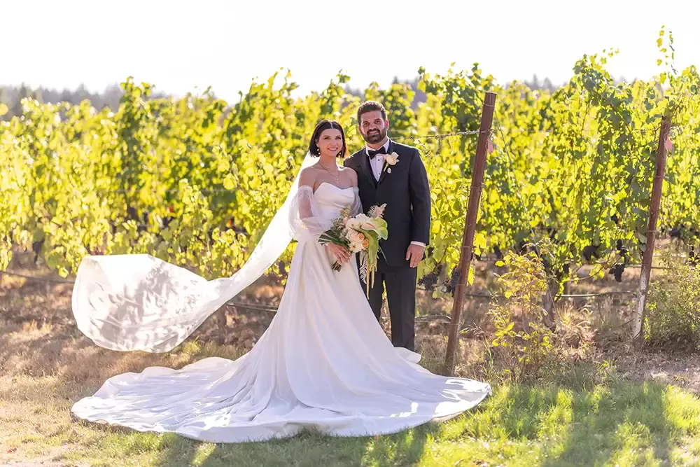 In the vineyard after the wedding ceremony bride and groom stand in the sunset light.