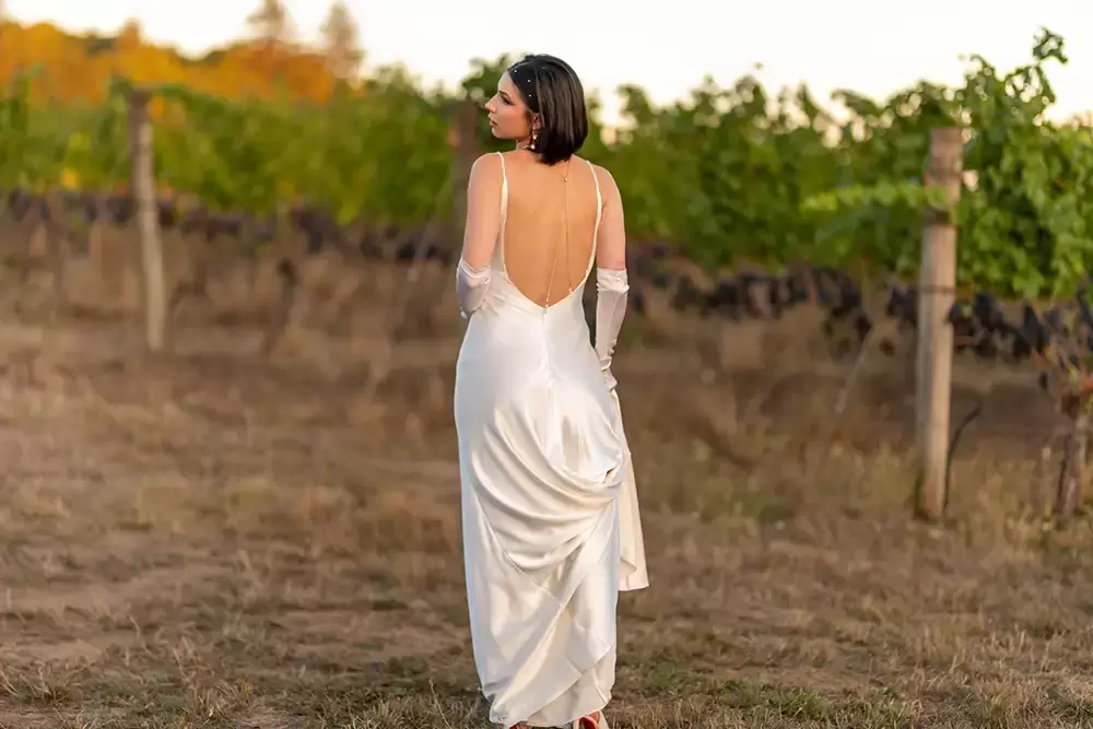 a bride stands in the vineyard showing off the back of her wedding dress 