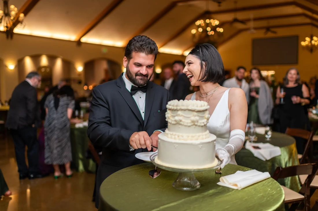 Bride laughs with the groom as he works on cutting the cake. 