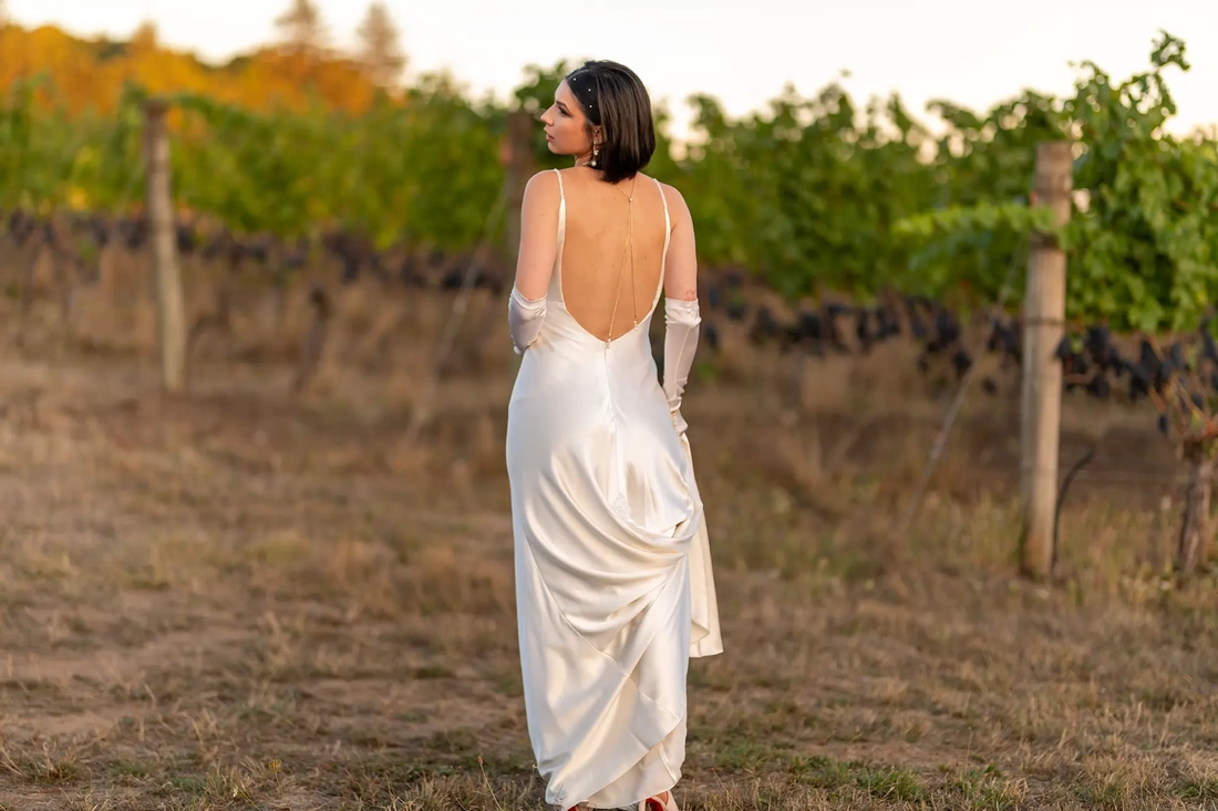 Bride standing in the vineyard showing off the back of her wedding dress