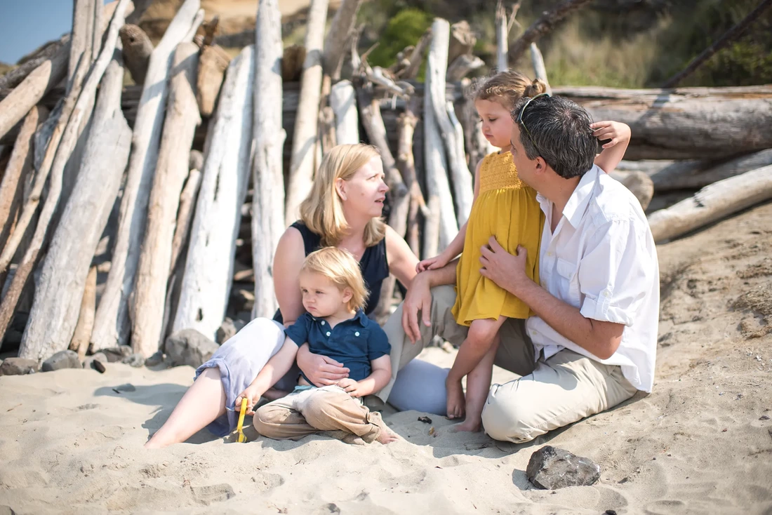 family picture at the beach A family sits together on the beach, behind them a structure made of driftwood logs.  Family Pictures Beach Theme with Portland Family Photographer Robert Knapp
