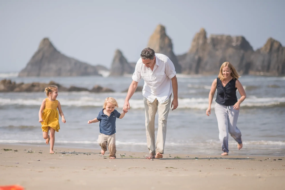  Family Picture on beach A family runs on the beach together, jagged rocks are behind them rising from the waves Family Pictures Beach Theme with Portland Family Photographer Robert Knapp